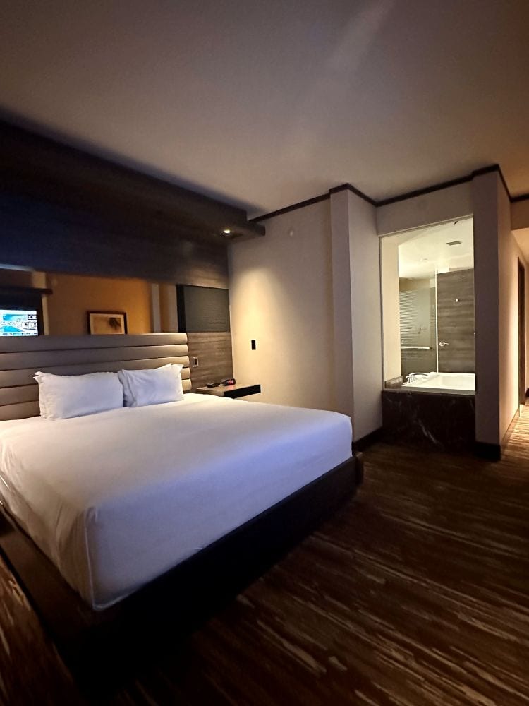 A guest room, the bed in the foreground, a window to the bath beyond, at the M Casino Resort, one of the best hotels in Las Vegas off the Strip.