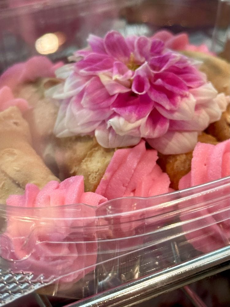 A pastry with pink icing and a pink flower on top at Creme de la Creme Albuquerque.