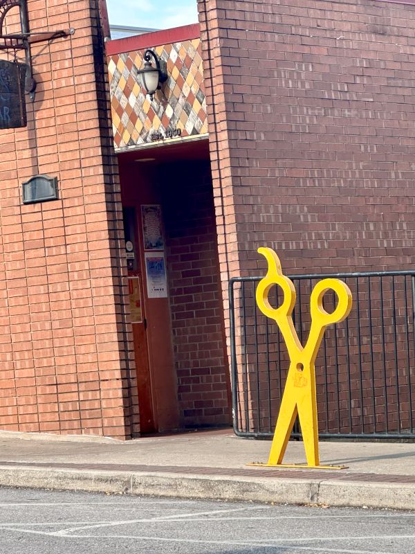 Yellow scissors sculpture stanging on their points on the sidewalk outside a hair salon in downtown Fayetteville Arkansas.