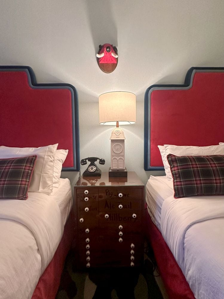 Two double beds with light blue walls and red headboard, and plaid pillows at The Graduate Hotel, in downtown Fayetteville, Arkansas.