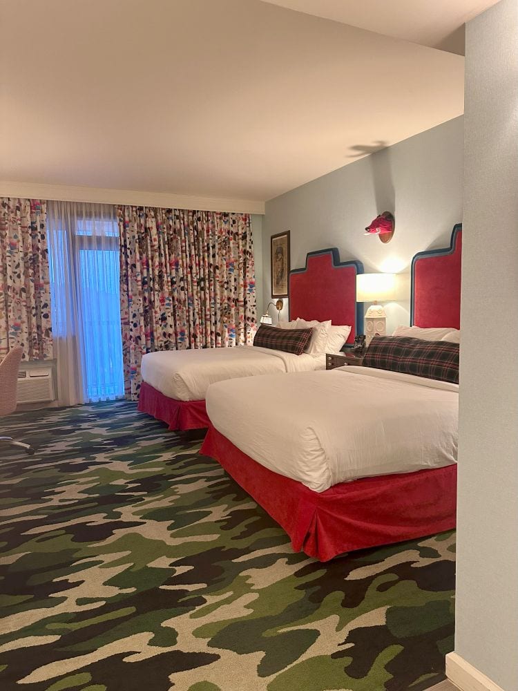 A guest room at the Graduate Hotel Fayetteville, Arkansas, with two double beds, red headboards, and camouflage carpet.