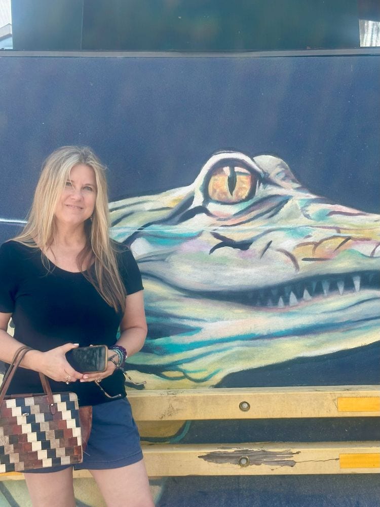 Bev standing in front of a an aligator painted on a wall in historic downtown Mount Dora.
