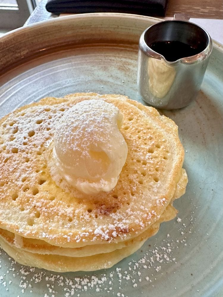 A stack of fluffy pancakes with butter on top and syrup on the side at Prelude Breakfast Bar, place place for breakfast in Fayetteville, Arkansas.