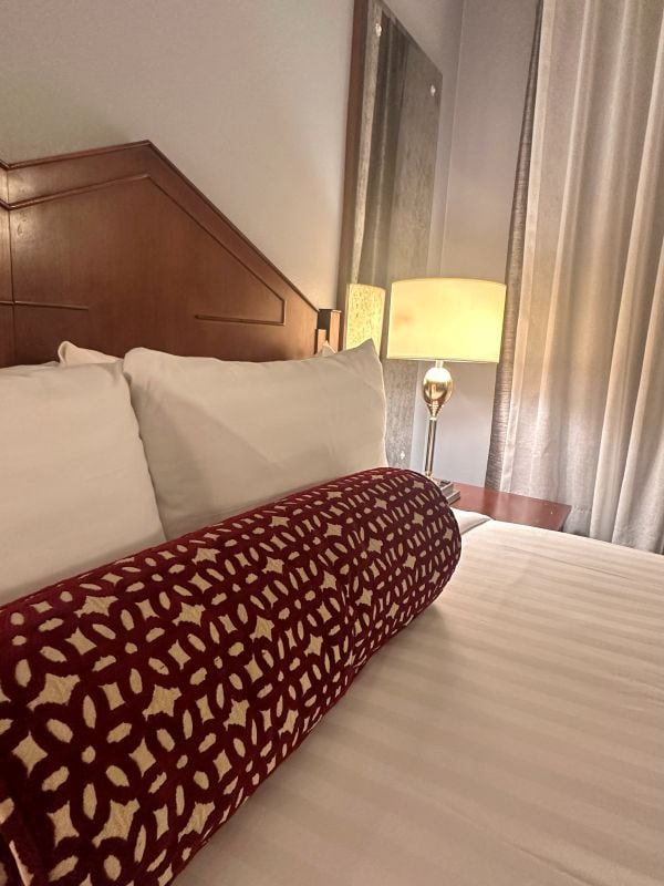 A bed and pillows with the lamp inthe background at the Biltmore, a haunted LA hotel.