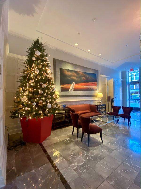 A lit Christmas tree in the lobby and a painting on the wall behind in front of a couch at The Alluvian Hotel in Greenwood, MS, a cozy holiday stay.