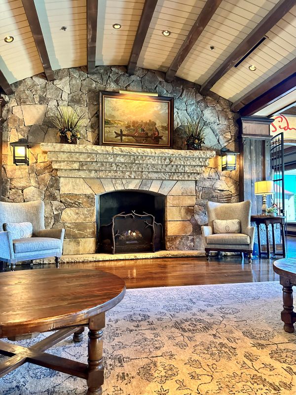 The large fireplace hearth made of stone and the wood rafters above in the lobby of Legacy Lodge, a cozy holiday stay.