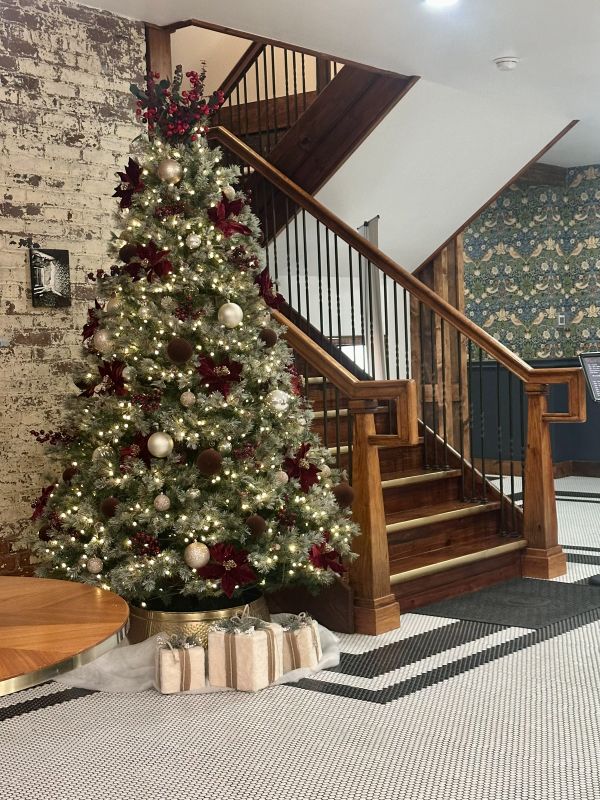 A Christmas tree in the lobby next to a wood staircase at The Chandler Hotel, a cozy holiday stay in Madison, Indiana.