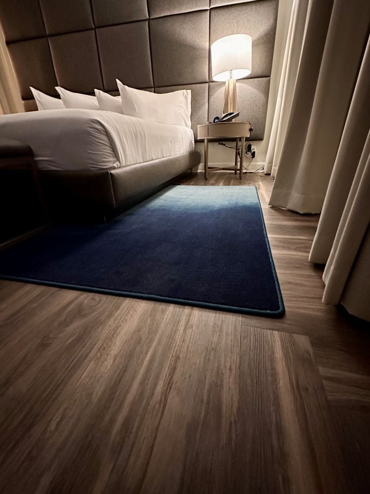A guest room view with light brown wood floors, looking at the bed with white plush bedding, neutral curtains along the windows at Hotel Deco, one of the best hotels in Omaha.