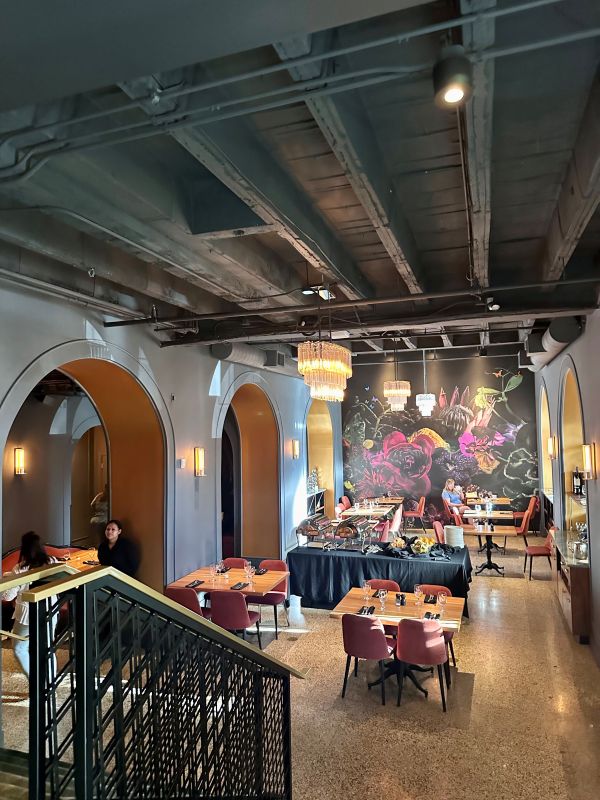 Look down from the top of the steps into Monarch Restaurant with a dark black with pinks mural along the far wall and tables in between, at Hotel Deco, one of the best hotels in Omaha.