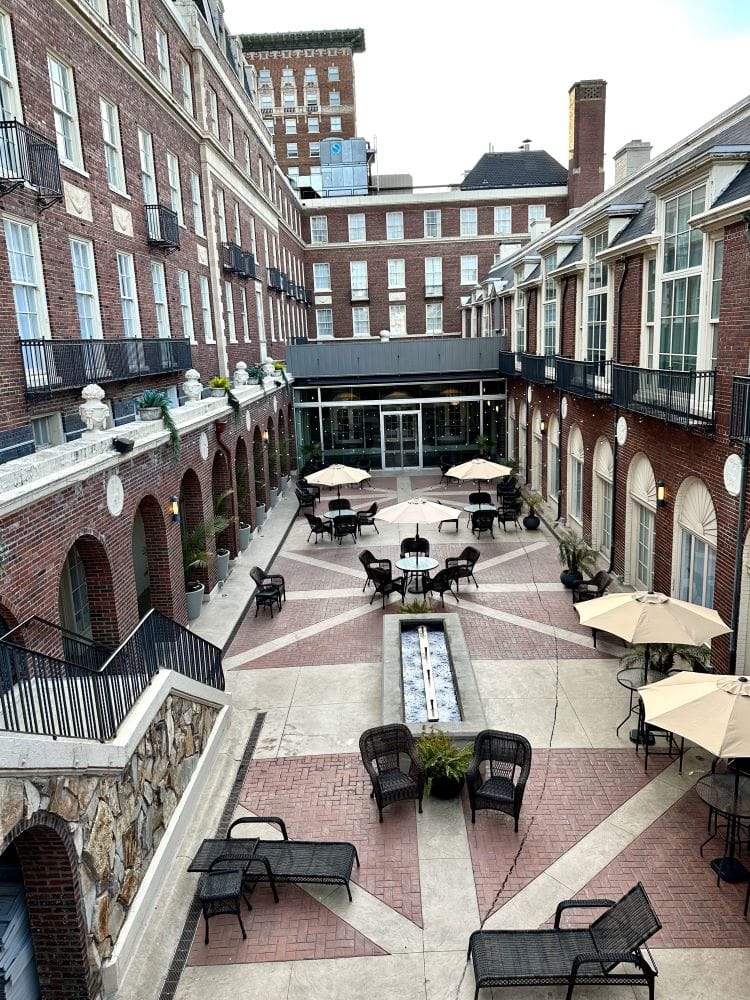 Looking down into the courtyard, with tables, chairs, umbrellas and surrounding by the building, at the Magnolia Hotel, one of the best hotels in Omaha.