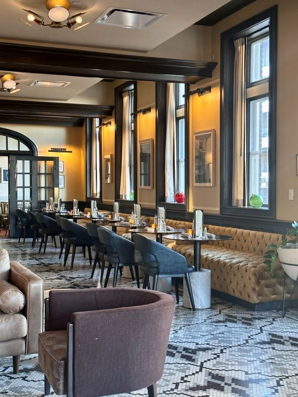 A view inside a restaurant with historic black and white tile floors, woodowrk on the ceiling and floors, warm colors at The Kimpton Cottonwood Hotel, one of the best hotels in Omaha.