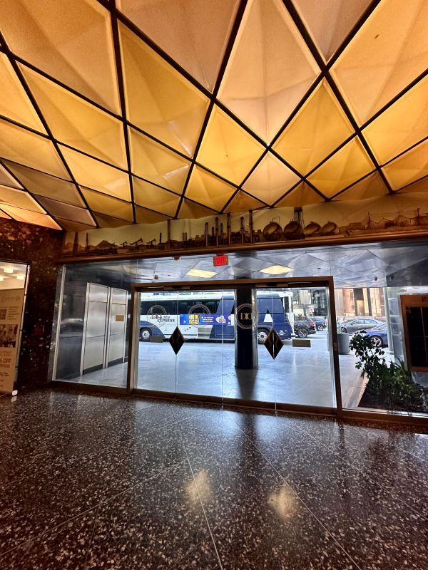 The original front entrance of the original Superier Oil HQ, with a geometric shaped backlit warm toned ceiling and a metal skyline of an oil field above the door, now The Delphi hotel, a boutique hotel downtown Los Angeles.