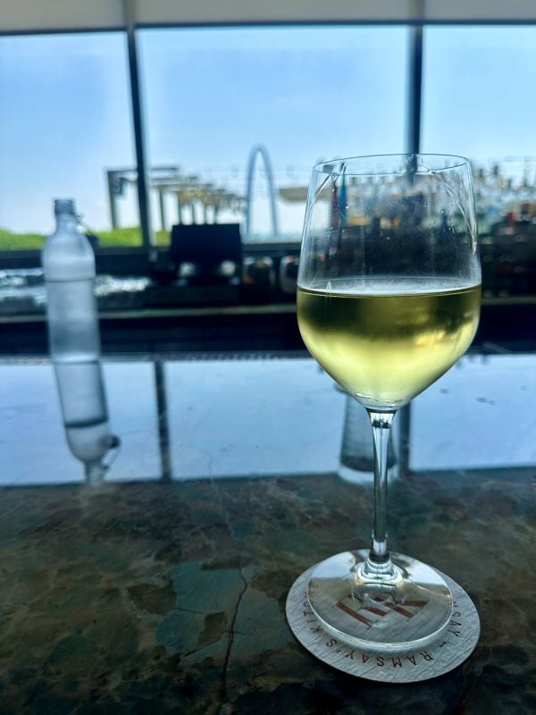 A glass of wine on the bar looking out through the glass windows to the St. Louis Arch.