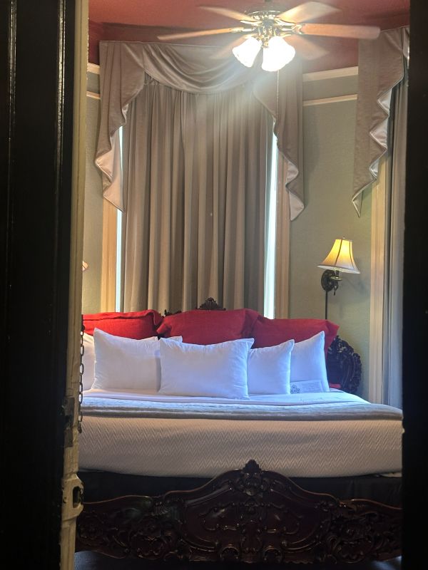 A peek through the door to a kind guest room, white pillows, soft green walls, poster bed, red headboard at the 1886 Crescent Hotel Eureka Springs.