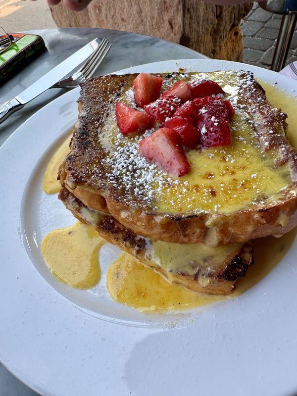 A plate of French Toast topped with a yellow syrup and strawberries at Petite Chou Bistro and Champagne Bar a local restaurant for breakfast in Indianapolis.