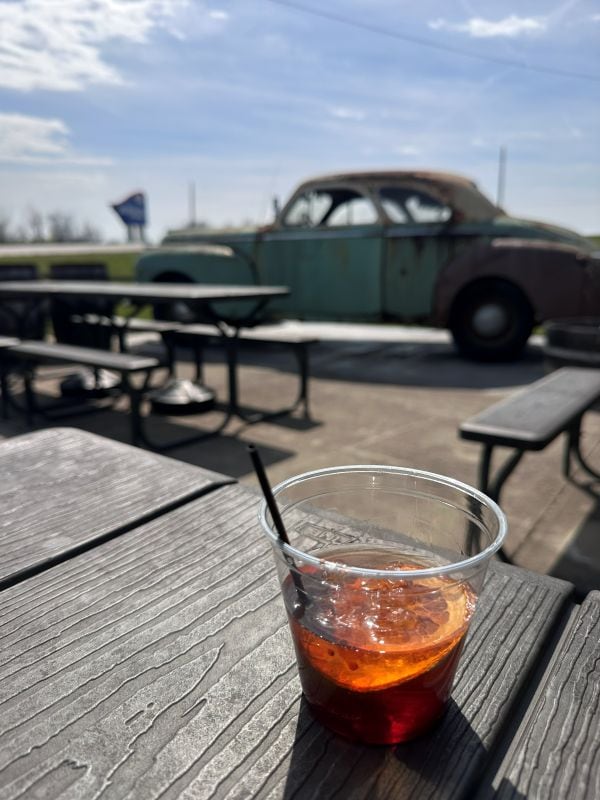 An Old Fashioned sitting on the picnic table outside with the old Chrysler in the background at Neeley Bourbon.