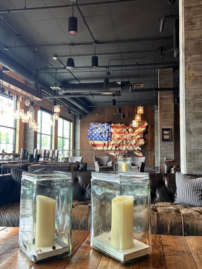 Hotel lobby, large industrial sized windows on left, flag shaped as the US map in the background wall, columns on the right side, and candles on the table in the foreground at the Ironworks Hotel, an industrial style hotel in Indianapolis.