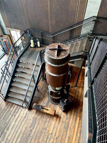 A steel staircase with a large industrial tower of some sort as decoration in the middle that leads to the lobby of the Ironworks Hotel, an industrial style hotel in Indianapolis.
