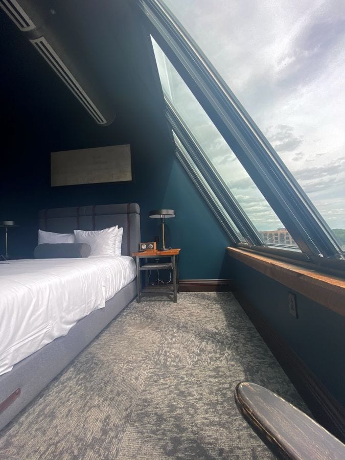 A low view from the end of the bed and the row of large angled windows in a guest room at the Ironworks Hotel, an industrial style hotel in Indianapolis.