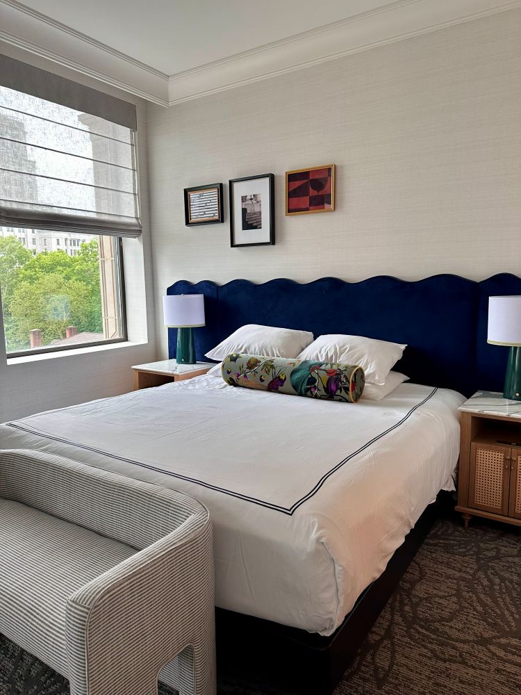 A guest room, white walls, white comforter, large windows and a blue velvet headboard at Kimpton Hotel Monaco.