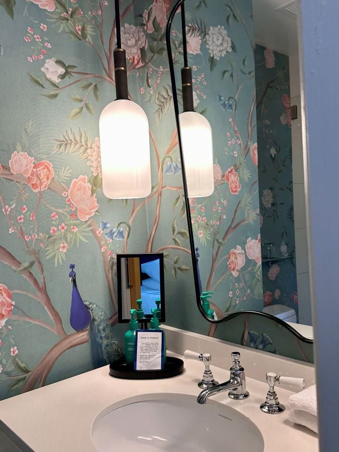 The bathroom with blue and pink floral wallpaper and a pendent light hanging at the Kimpton Monaco, a hotel near Independence Hall.