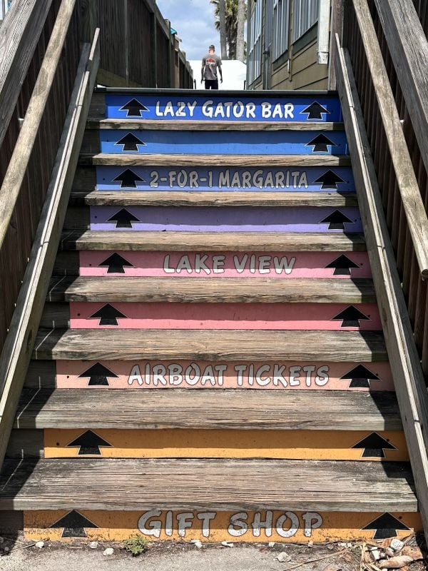 The wood steps leading to the Lazy Gator Bar painted different colors and words written on them, like "Lazy Gator".
