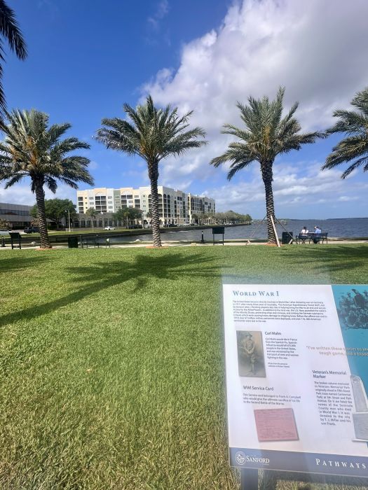 A historical marker about World War I in the foreground and palm trees, the lake and a new white building in the background in Sanford Florida.