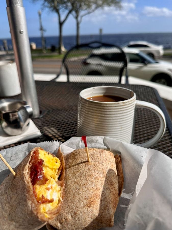 Coffee and an egg burrito on the table with the lake in the background outdoors at Caffe Di Riverwalk in Sanford Florida.