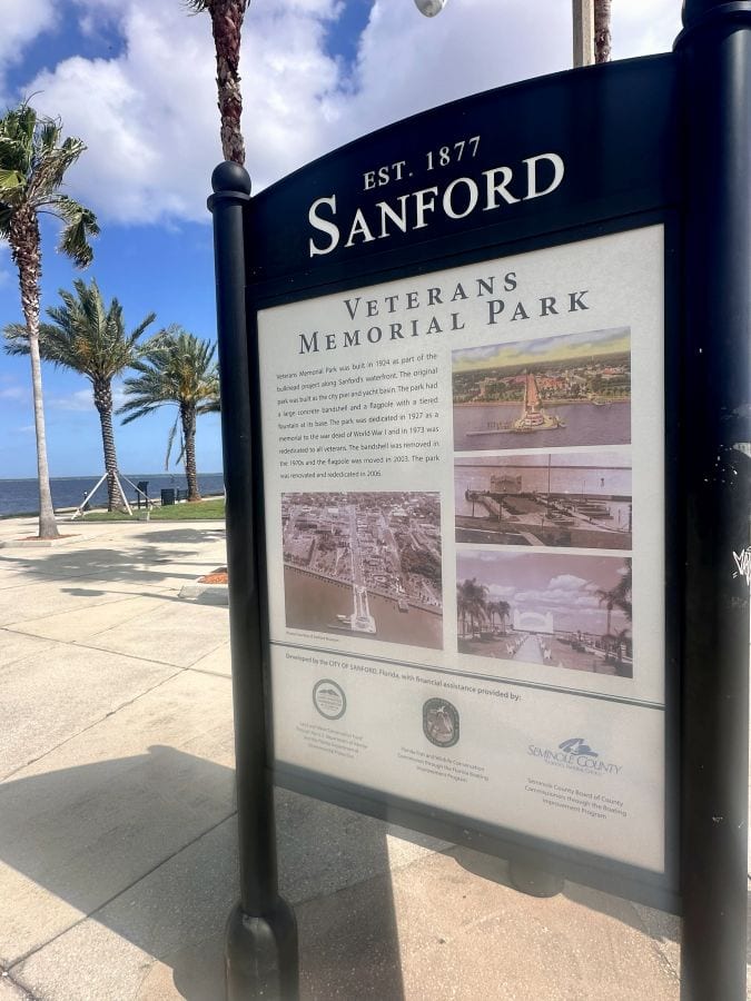 A Sanfdford Florida sign with history of the town on it and palm trees in the background in Sanford Florida.