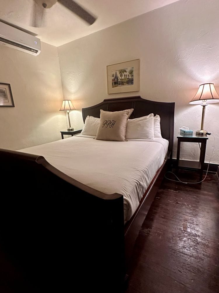 A queen bed with white bedspread, antique wooden headboard and footboard in a guest room at the Park Plaza Hotel, a Winter Park Florida Hotel.