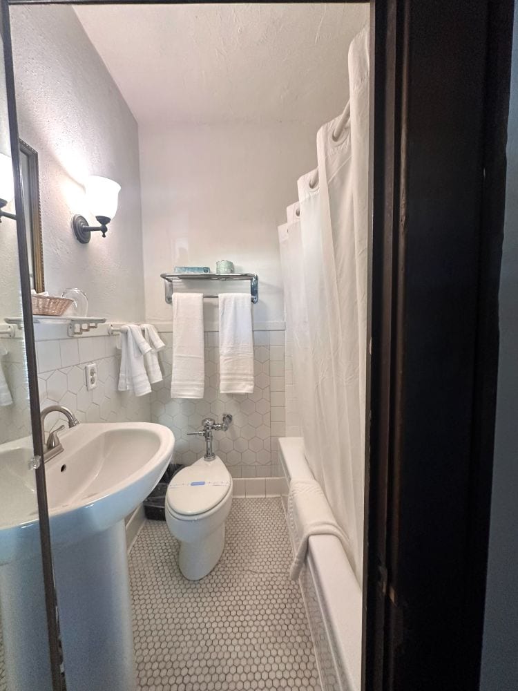 A bathroom in a guest room, with a pedestal sink, tuba dn shower and toilet, pretty tight fit, all white at the Park Plaza Hotel, a Winter Park Florida hotel.