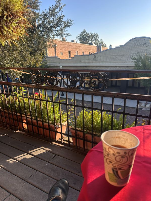 A cup of coffee on a table with a red table cloth and a iron banister in the background on the balcony with morning sunlight at the Park Plaza Hotel, a Winter Park Florida Hotel.