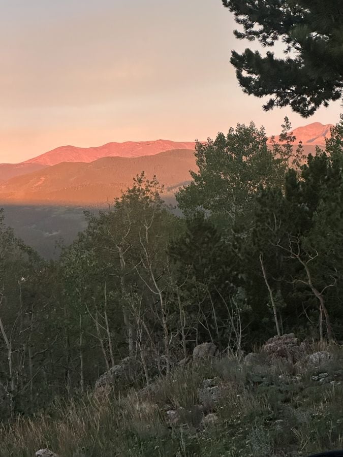 A view of the mountains from our Airbnb, trees in the foreground and a red cast on the mountain range in the background on my Colorado Mountain retreat.