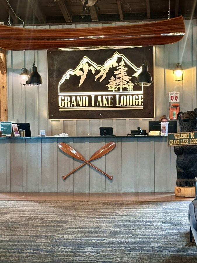 The lodge reception desk with the large metal rusty colored Grand Lake Lodge sign.