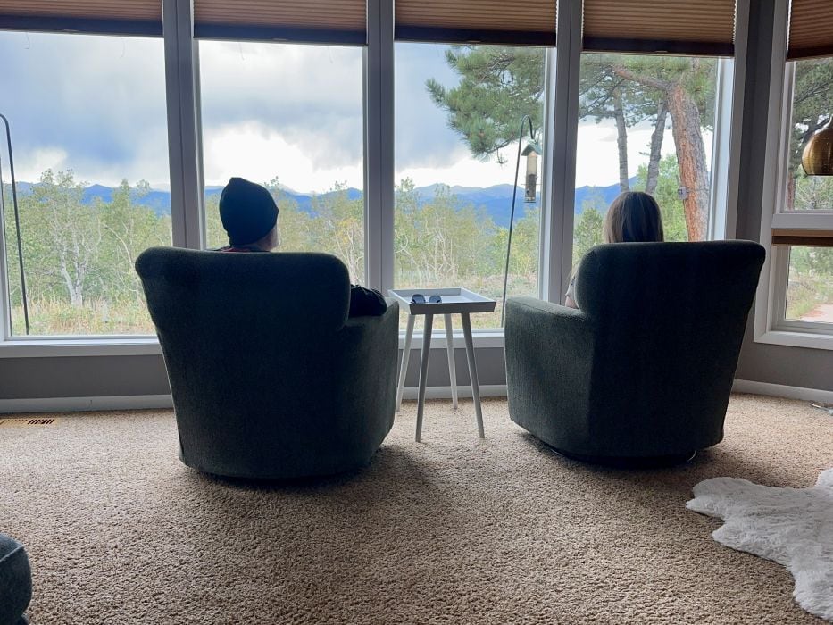 the back of the chairs with me and my husband sitting in them looking out the windows to the mountain range at Alpina Haus on our Colorado mountain retreat.