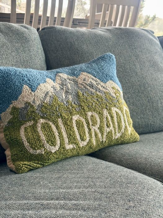 A pillow on the couch that says Colorado with a mountain on it.