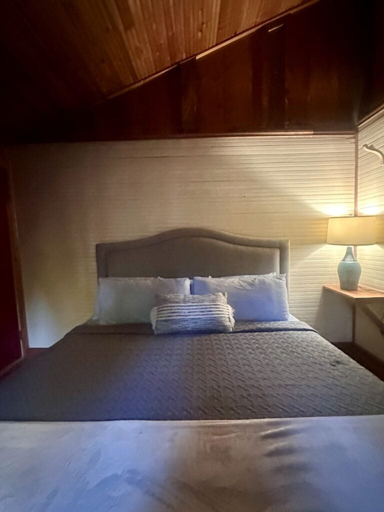My bed with warm lighting from a lamp on my room of the Firefly Cabin at the Brown Mountain Beach Resort.
