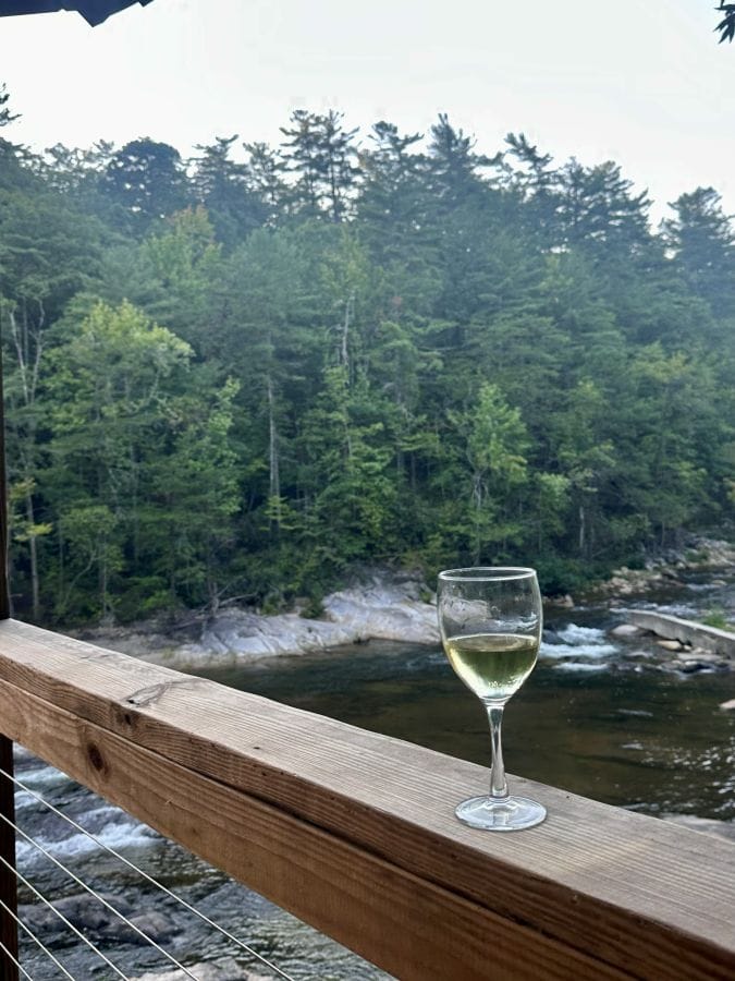 A glass of wine sits on the railing of the upper deck with views of the forest and creek at Brown Mountain Beach Resort.
