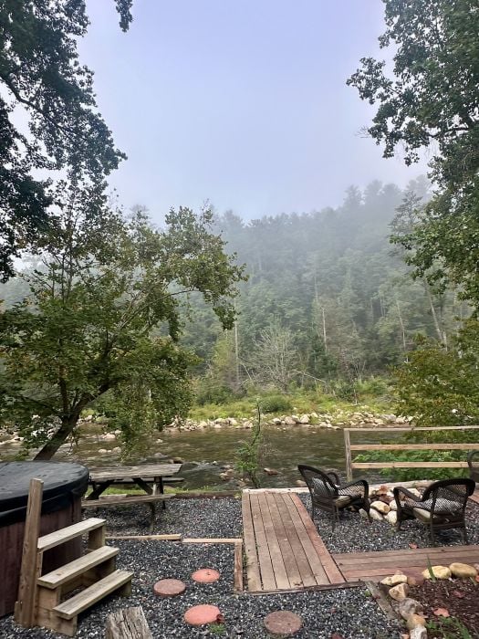 the backyard of the Firefly cabin, the creek, a hottub and grill pluss a sitting area with a fire pit at Brown Mountain Beach Resort.