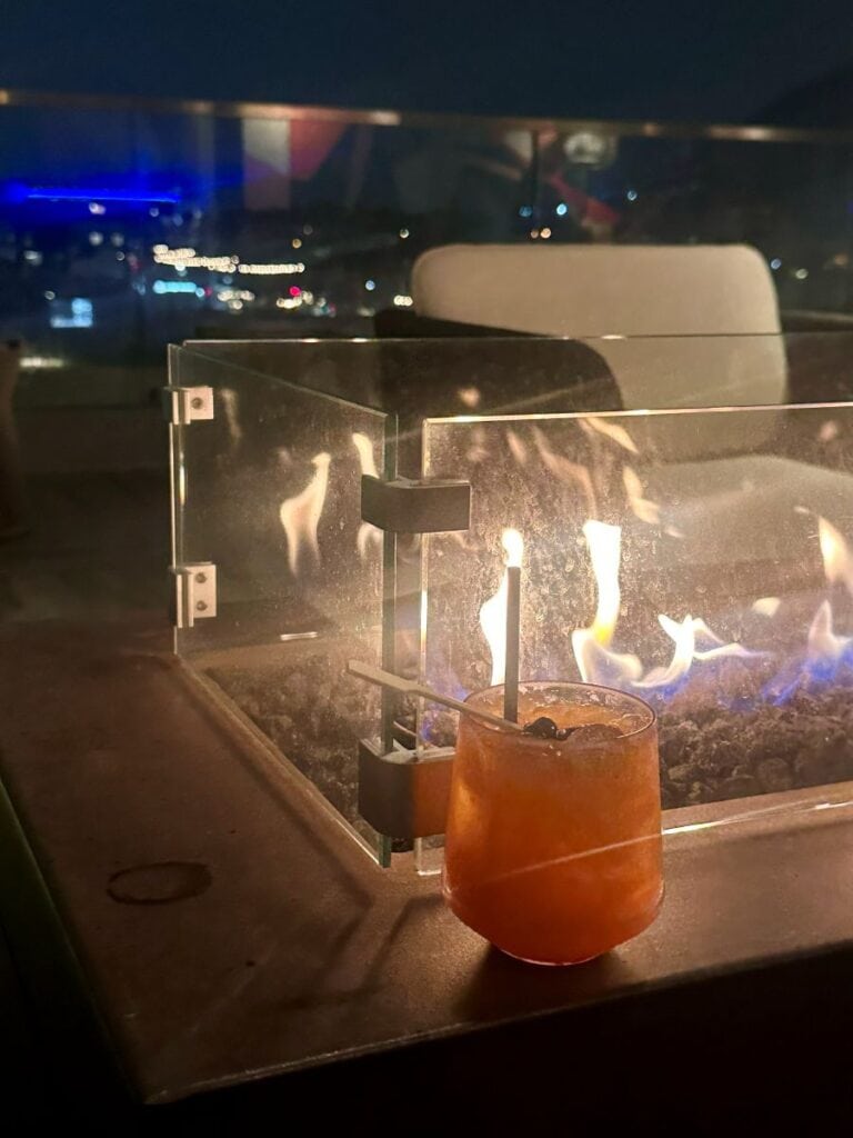 Glass of cocktail with a straw next to a modern fireplace at night at the Outsider Rooftop Lounge in Scottsdale, Arizona