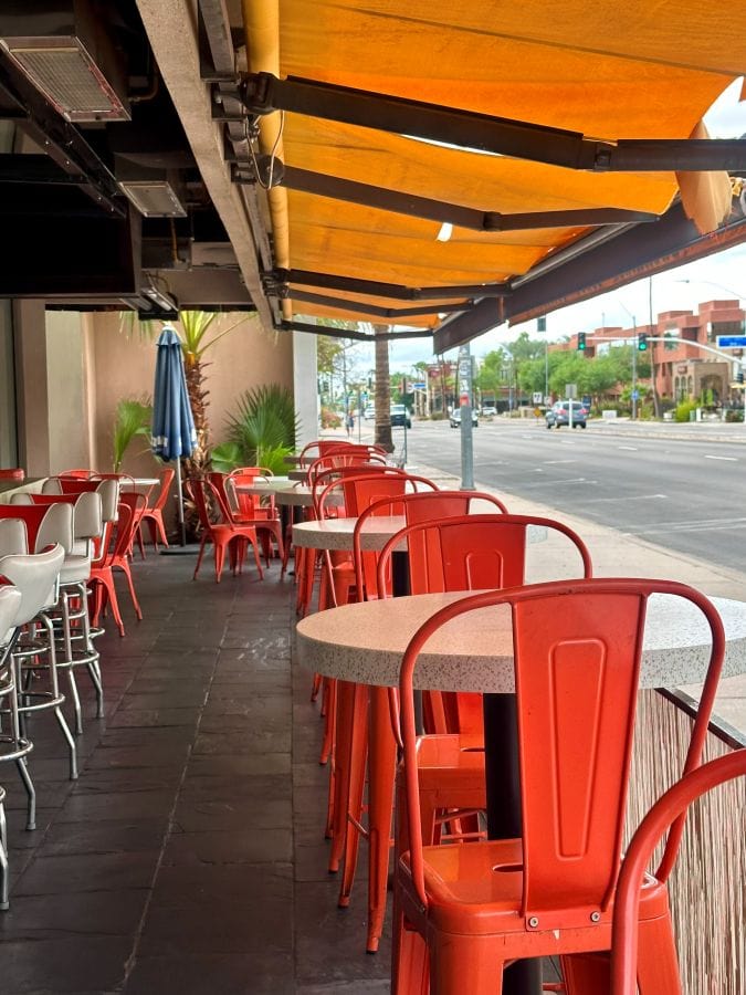 Colorful outdoor cafe seating with orange chairs and umbrellas at The Morning Squeeze in Scottsdale, Arizona.
