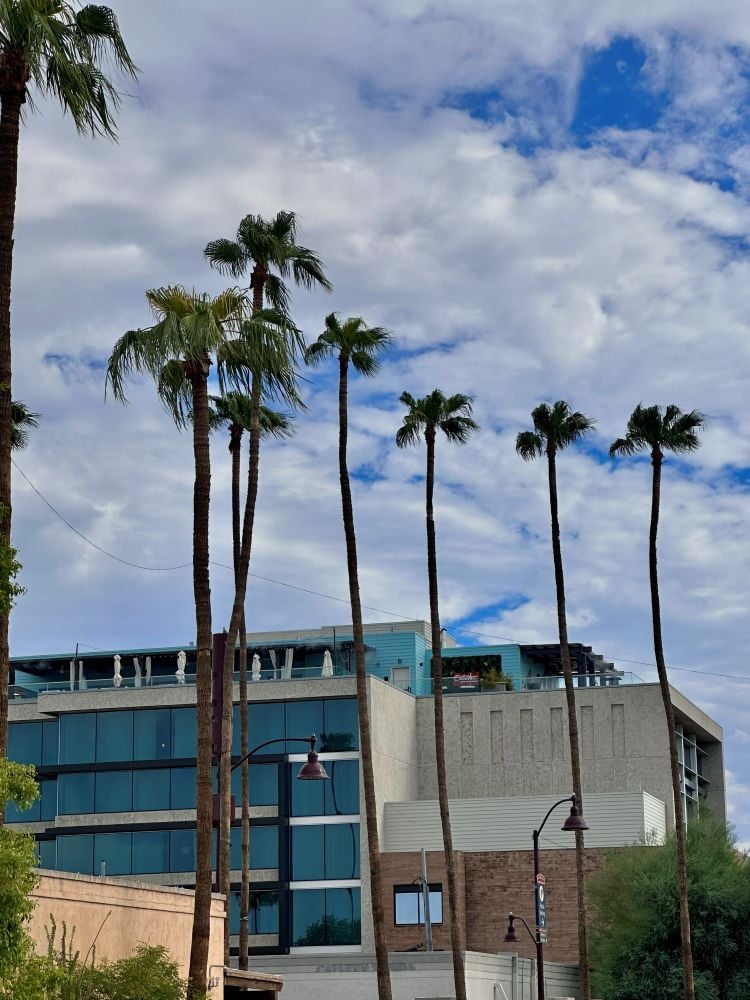 Modern hotel in Scottsdale with tall palm trees and a partly cloudy sky. The Outsider Rooftop Lounge sits on top in Scottsdale, Arizona.