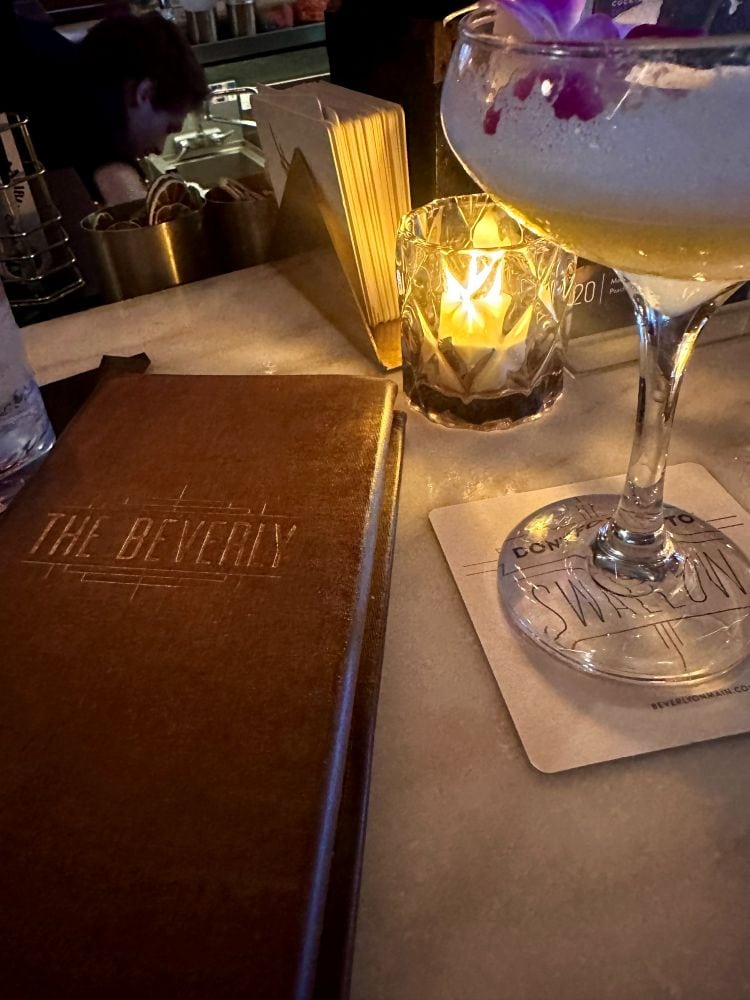 Cozy candle lighting with a coctail and the leather cocktail menu with The Beverly on it in Old Town Scottsdale, Arizona.