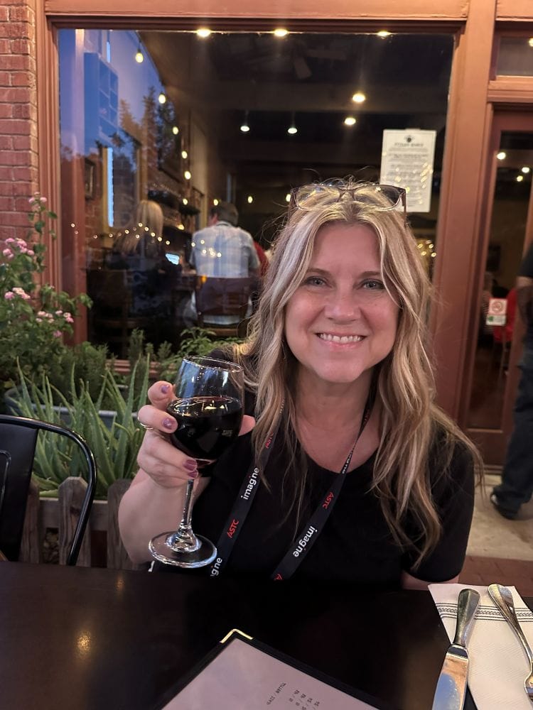 Woman with blonde hair holding a glass of red wine at a an outdoor table at Pizzeria Bianco in Phoenix, Arizona.