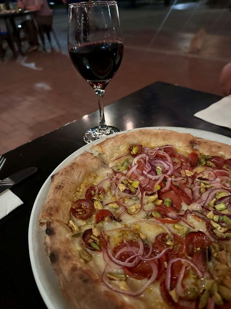 Fresh pizza with onions, peppers, and meat served with a glass of red wine at Pizzeria Bianco in Phoenix, Arizona.