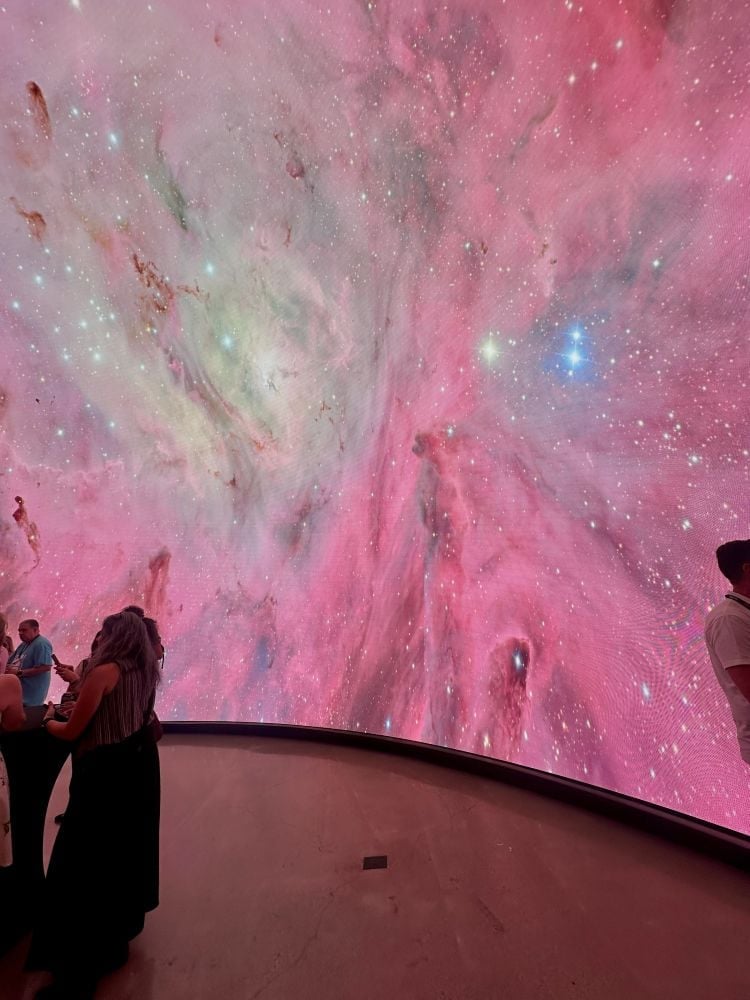 Vivid cosmic nebula projected on a large screen with visitors observing at the Arizona Science Center in Phoenix, Arizona.