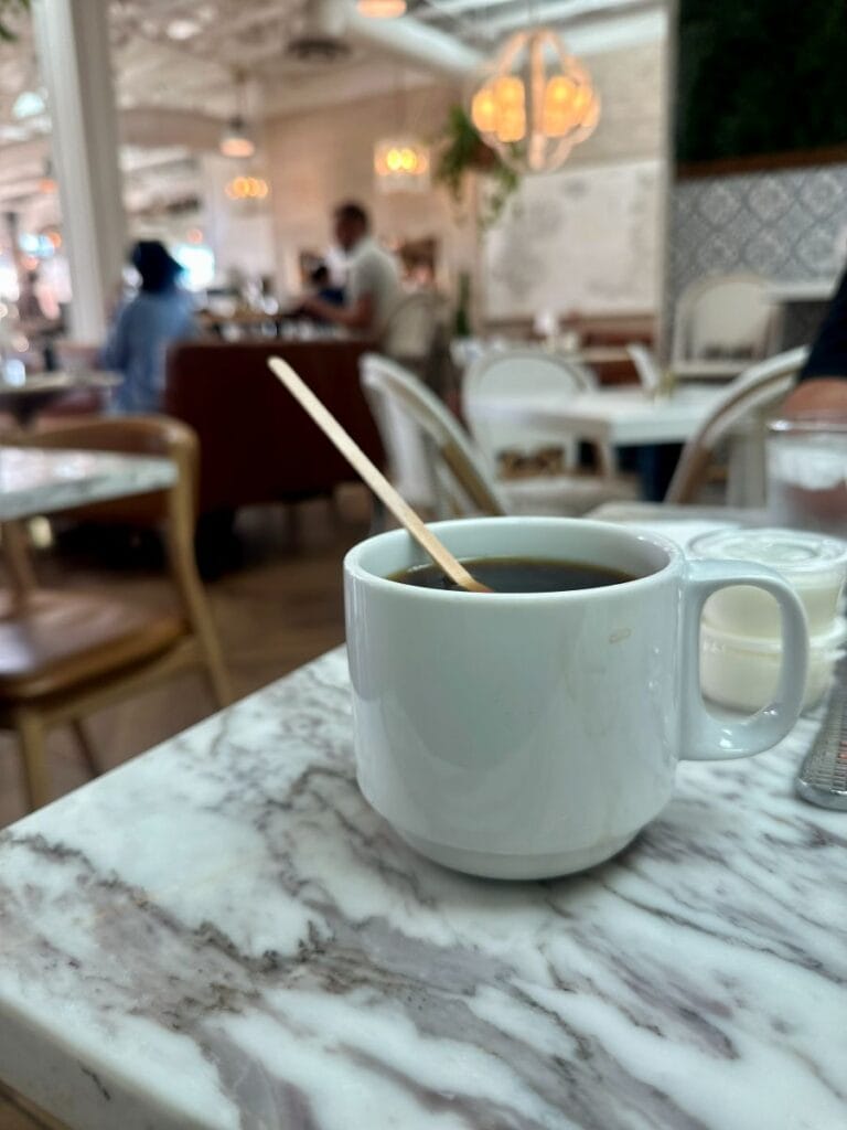 A steaming cup of coffee on a marble table in a bright cafe setting at JoJo Coffeehouse in Scottsdale, Arizona.