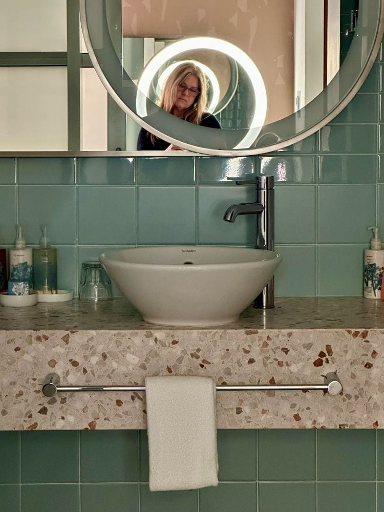 Woman taking a selfie in a bathroom with a circular mirror and green tiles at Hotel Valley Ho in Scottsdale, Arizona.