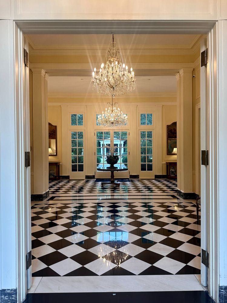 The front entrance door, looking in from the porch with black and white checkered floors and chandeliers at the Duke Mansion, one of the historic hotels in Charlotte.