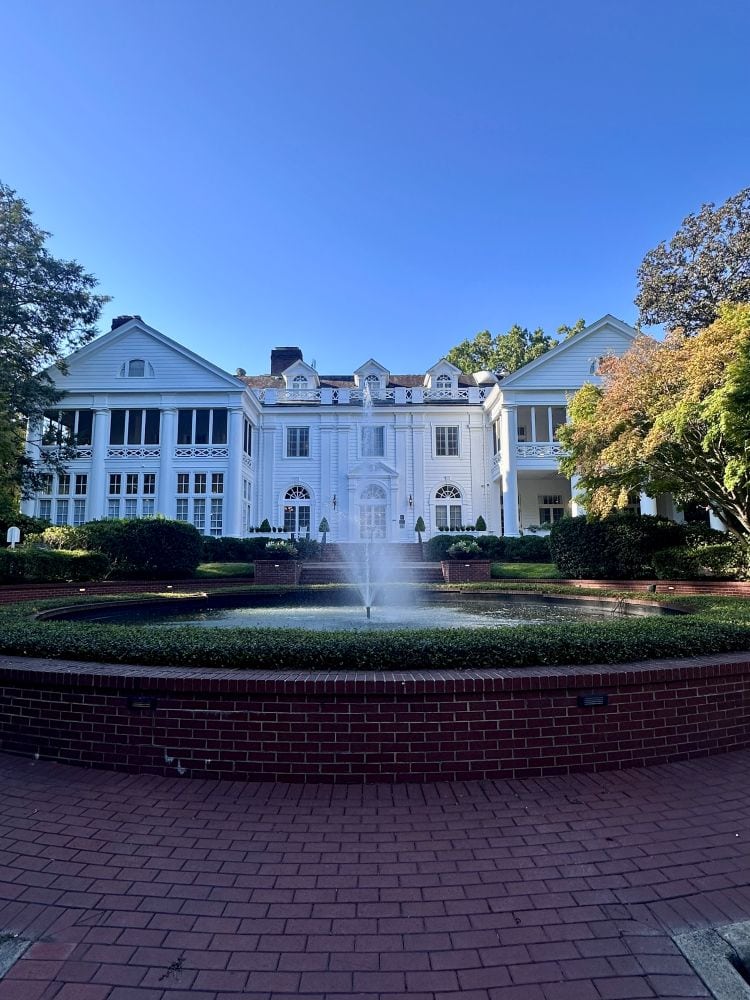 The front of the DUke Mansion, white with a large fountain in front, one of the historic hotels in Charlotte.